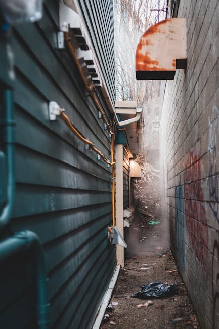 A narrow urban alleyway between two brick buildings, featuring a paved surface with double yellow lines running along each side. The left building has red-brown brickwork with small, sash-style window